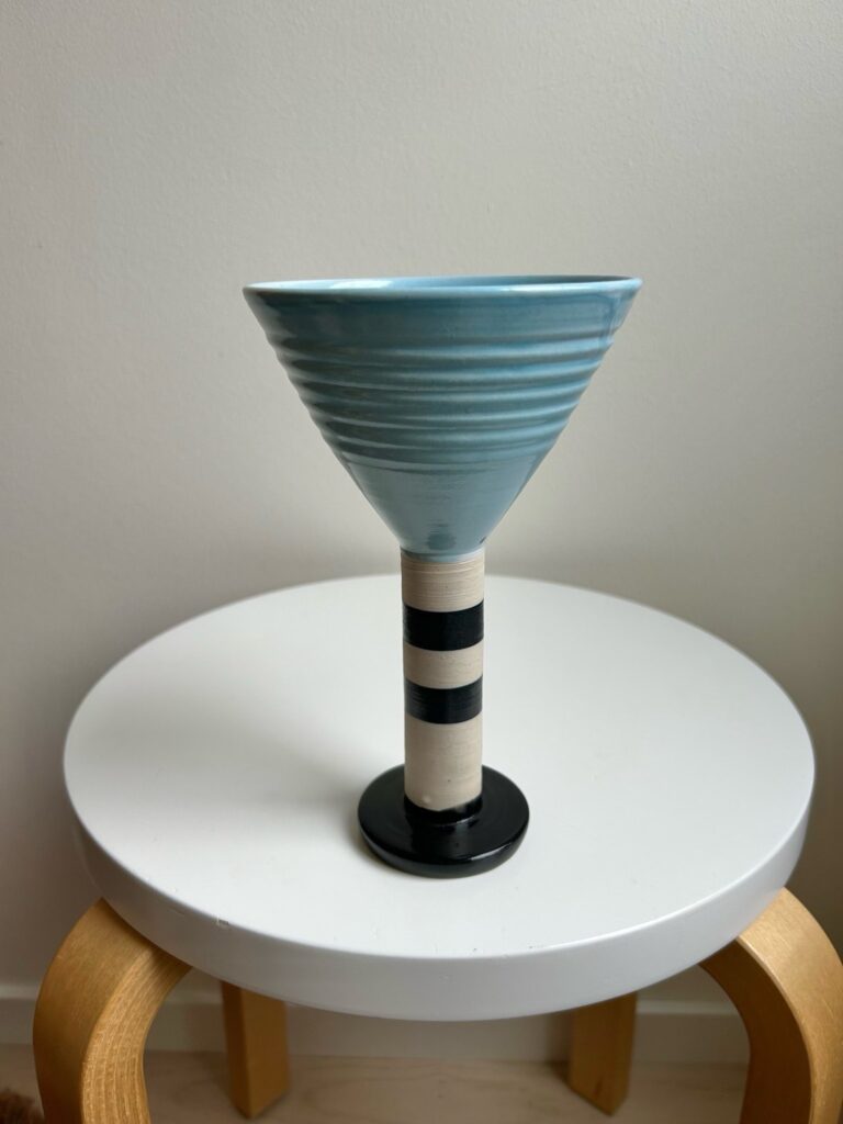 A blue and white striped ceramic drinking cup with a tall stem, placed on a white stool.
