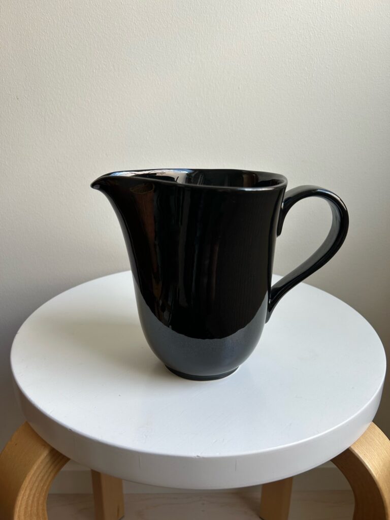 A black ceramic pitcher with a handle, positioned on a white stool.