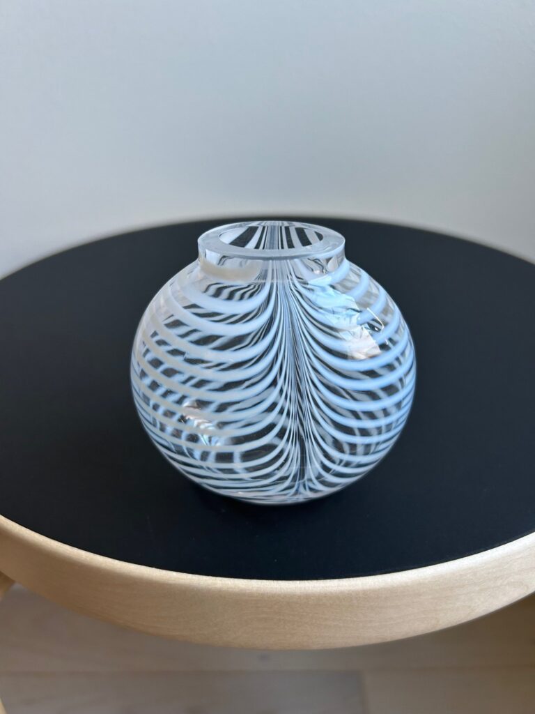 A small round glass vase with white swirling stripes, sitting on a black circular surface.