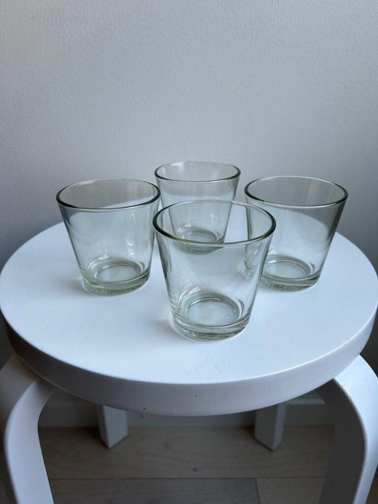 Four clear glass tumblers arranged on a round white stool.