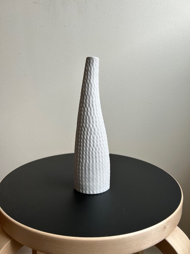 tall white ceramic vase with a textured reptile-like surface pattern, placed on a black round stool