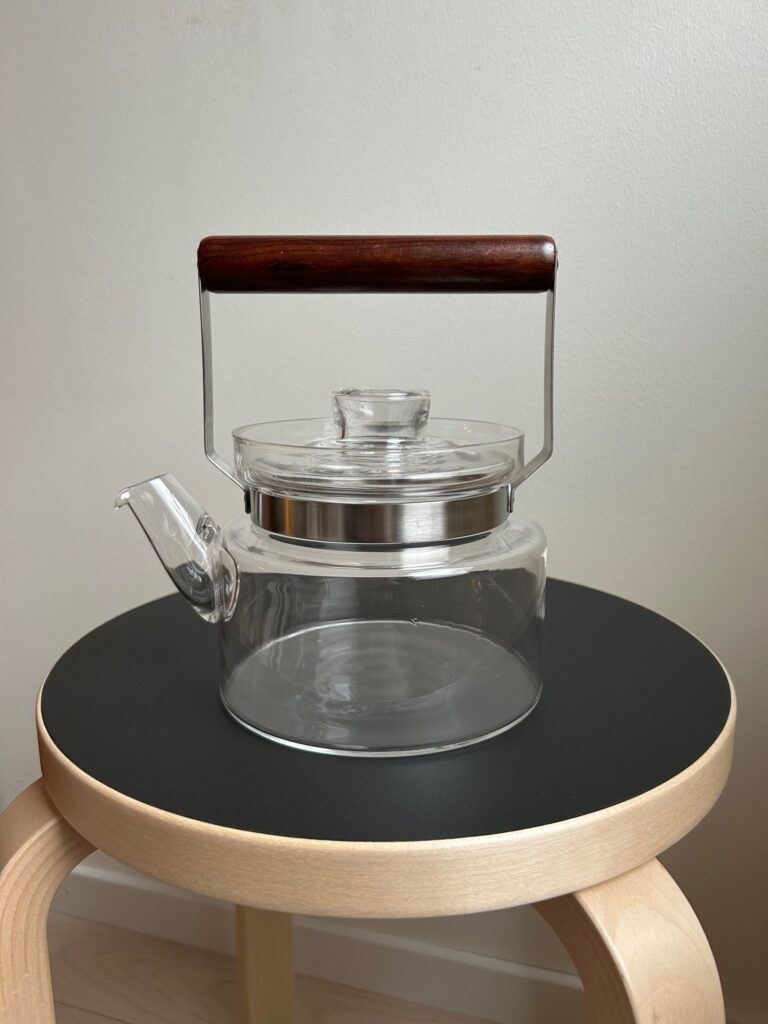 Clear vintage glass teapot with a teak wooden handle and metal frame, designed in a minimalist Scandinavian style