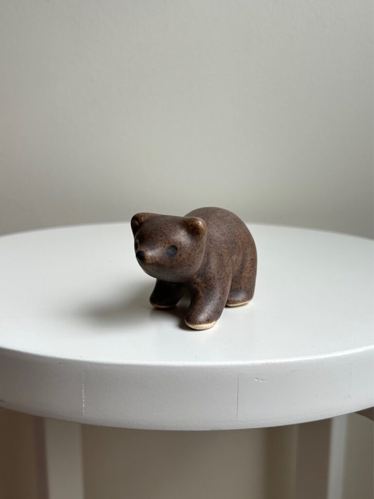 small brown ceramic bear figurine standing on a white round stool