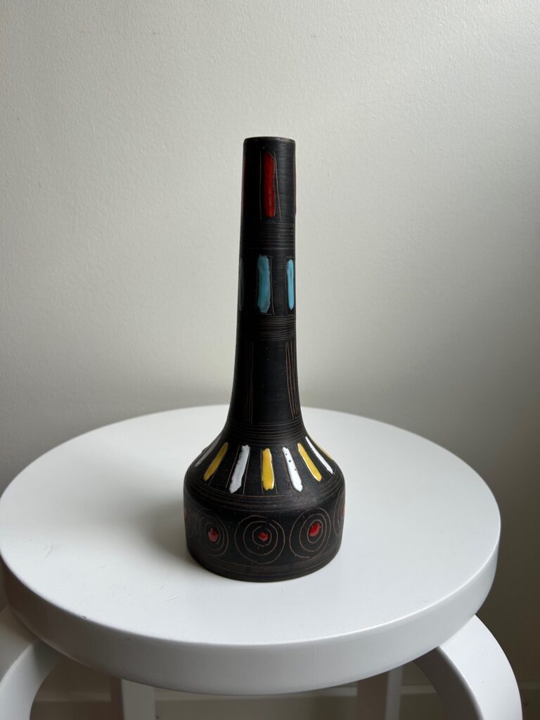 tall dark ceramic vase with colorful geometric accents near the neck, standing on a white stool