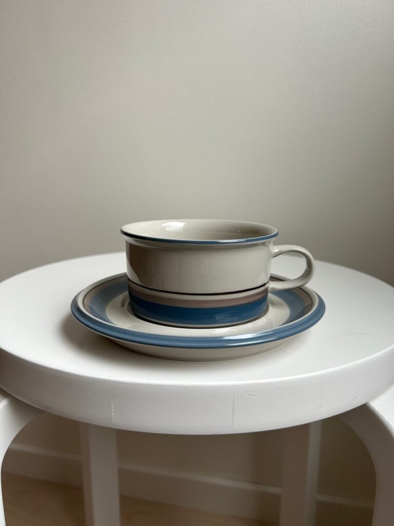 grey and blue ceramic teacup with matching saucer, placed on a white stool