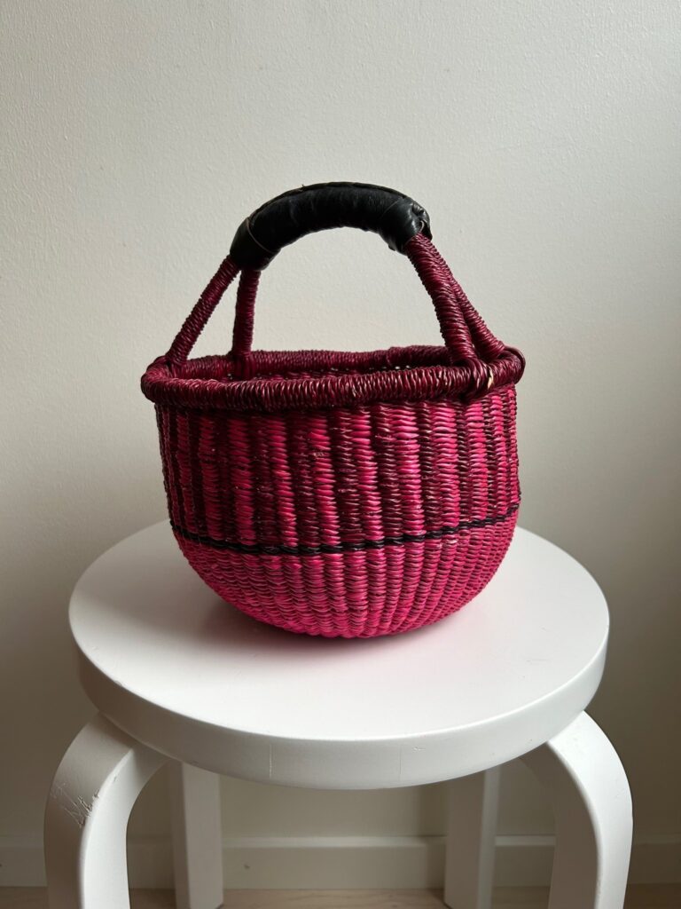 Handwoven pink Bolga basket with black accents and a wrapped handle, photographed as a decorative home piece