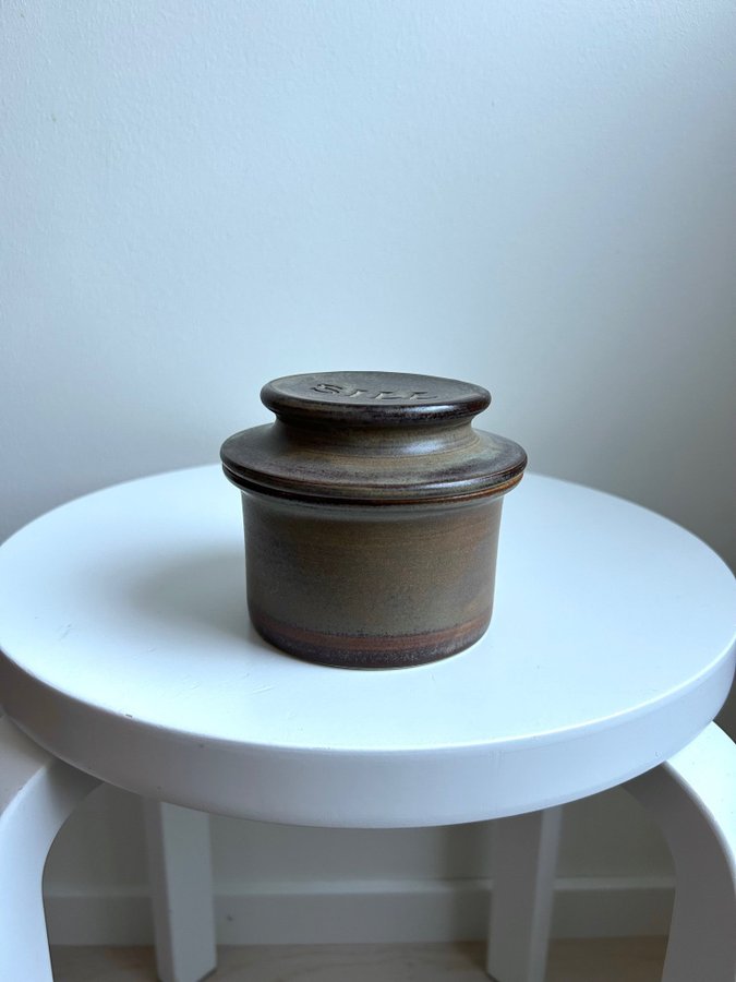 small brown ceramic storage jar with lid, placed on a white stool