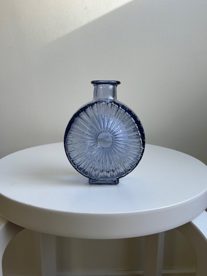 flat round blue glass vase with radiating sunburst pattern, displayed on a white stool
