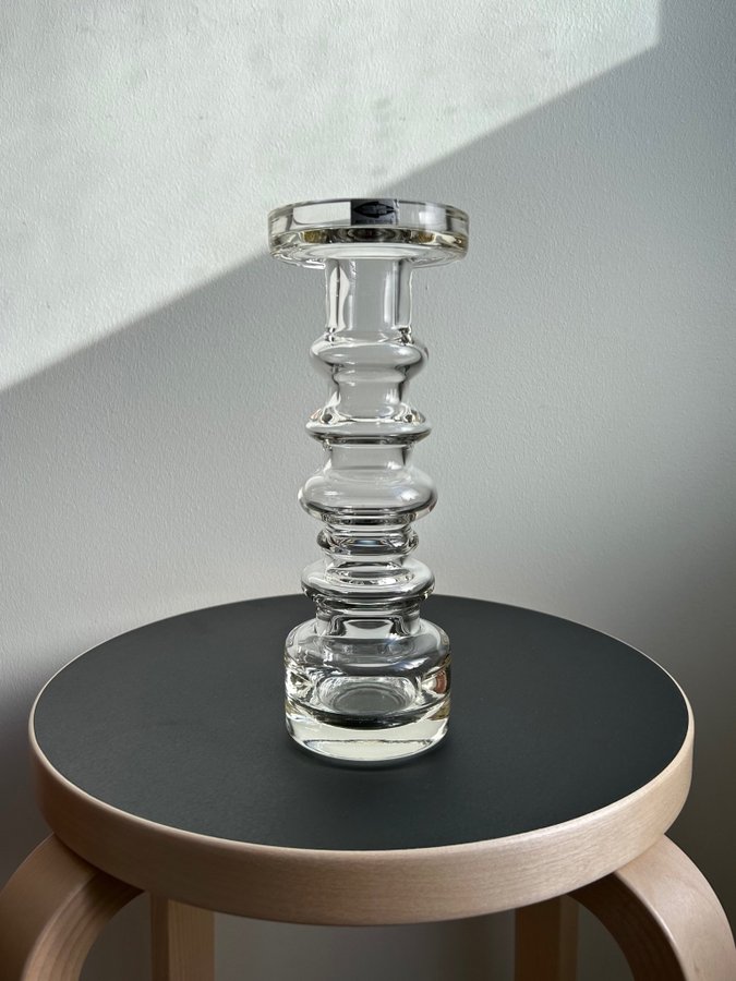 tall clear glass candle holder with stacked circular rings, placed on a black stool
