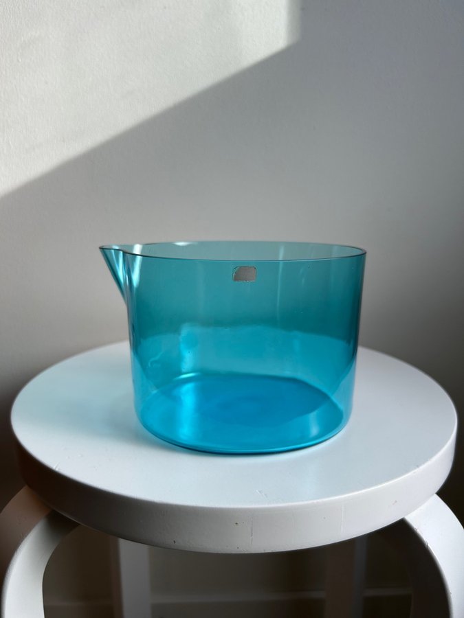 round turquoise-blue glass bowl with a slightly curved rim, placed on a white stool